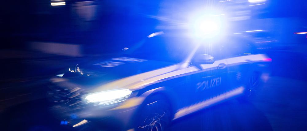 Ein Polizeifahrzeug fährt im Rahmen eines Fototermins mit Blaulicht an einem Gebäude vorbei.