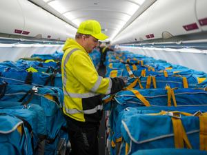 Vor dem letzten Postflug befestigt ein Mitarbeiter der Wisag auf dem BER in einem Airbus A320-214 mit Stoffmanschetten abgedeckte Plastikboxen voller Briefe und anderer Post auf den Passagiersitzen. 