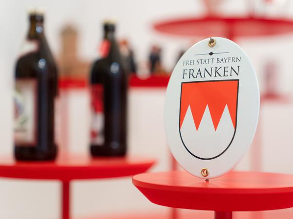 Bierflaschen und ein Schild mit der Aufschrift „Frei statt Bayern - Franken“ auf der Bayerischen Landesausstellung in Ansbach. 
