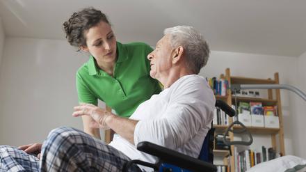 Eine Pflegerin spricht mit einem Mann im Rollstuhl.