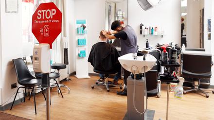 Der Friseur Noor Agha Karimi frisiert einen Kunden in dem Friseursalon Mac Hair in Wannsee. In Salon steht ein Schild mit der Aufforderung, die Hände zu desinfizieren. Angesichts der Omikron-Welle hat der Berliner Senat einige neue Corona-Regeln beschlossen. Die Verordnung ist seit dem 05.02.2022 in Kraft. +++ dpa-Bildfunk +++