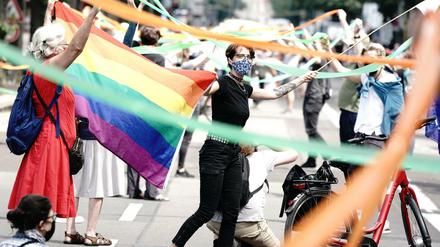 Teilnehmer der "Unteilbar"-Demo stehen mit Mundschutz und einer Regenbogenfahne nahe dem Brandenburger Tor.