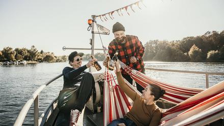 Drei Personen auf einem Boot prosten sich fröhlich mit Getränken zu.