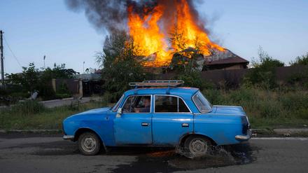 Ein Ukrainer fährt am 27. Juni 2022 an einem brennenden Haus in der Nähe von Bachmut vorbei.