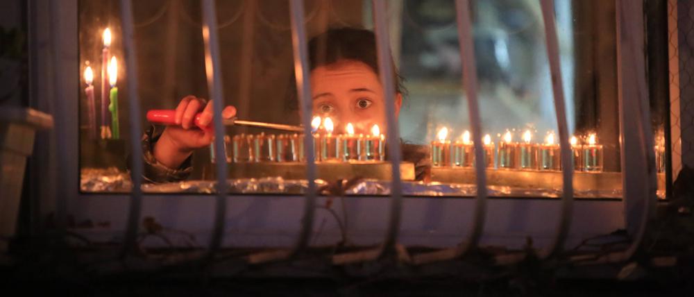 Lichterfest im Schatten des Krieges. Ein Mädchen zündet in Jerusalem eine Kerze auf der traditionellen Chanukkia an.