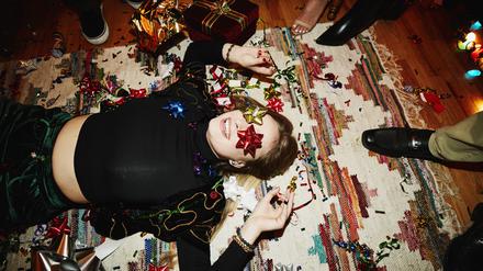 Laughing woman lying on floor with bows over eyes during holiday party with friends