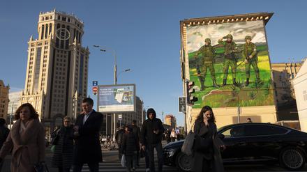 Vor dem Hintergrund einer Militärmalerei an einer Hauswand machen sich die Menschen in Moskaus Stadtzentrum auf den Weg in die Arbeit.