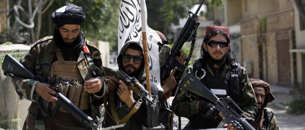 Schwer bewaffnete Taliban-Kämpfer patrouillieren nach ihrer Machtübernahme mit wehender Flagge des Islamischen Emirats Afghanistan durch Kabul.