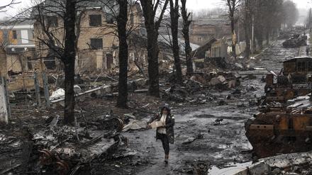 Eine Frau geht auf einer Straße, die überseht ist mit zerstörten russischen Militärfahrzeugen.