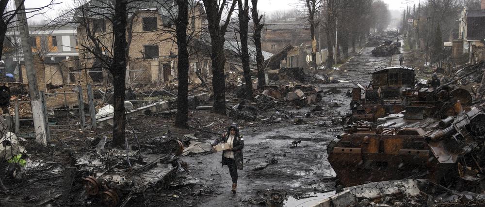 Eine Frau geht auf einer Straße, die überseht ist mit zerstörten russischen Militärfahrzeugen.