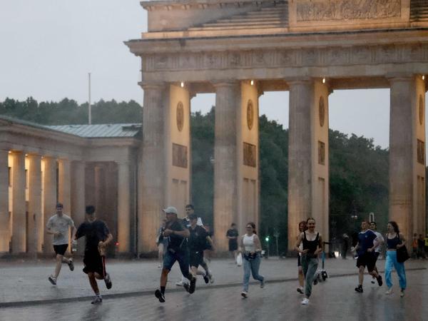 Passanten und Touristen werden vorm Brandenburger Tor am Pariser Platzrennen in Berlin von einem Unwetter überrascht (Archivbild).