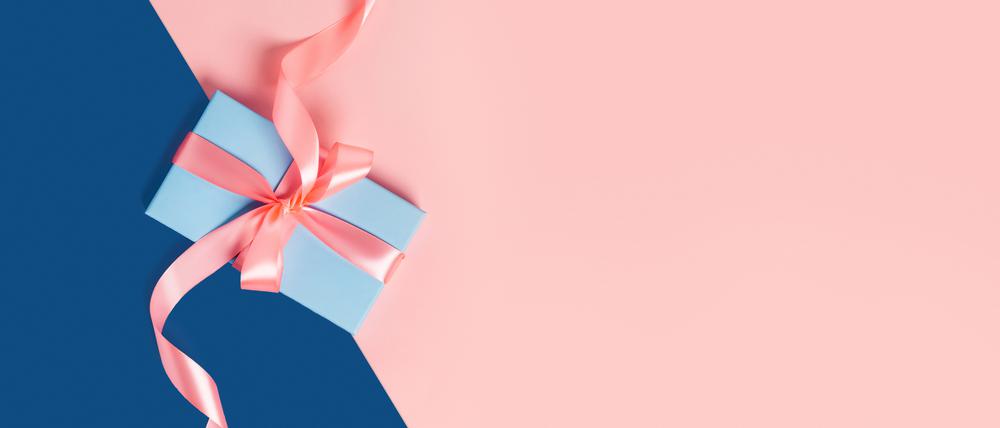 Greeting card with one gift box on classic blue background. Pink bows. Central composition. Flat lay, top view.