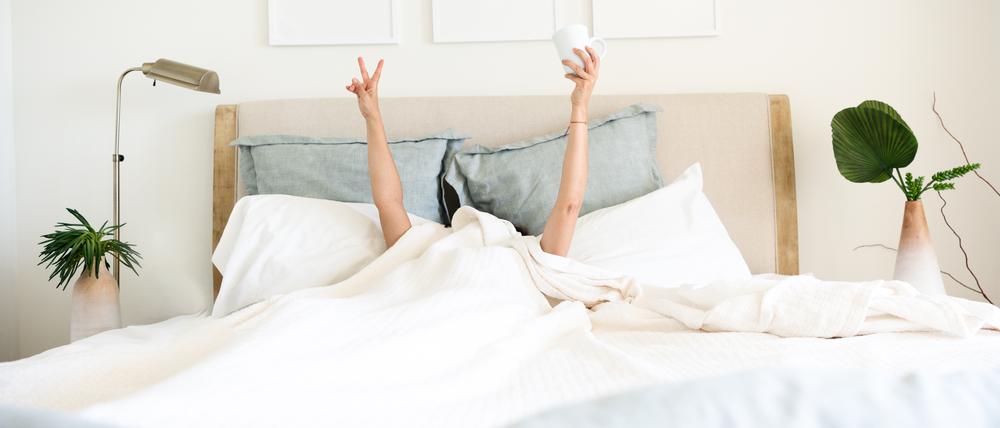 Hispanic mature woman waking up in bed with coffee mug in hand underneath the bed cover