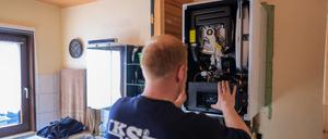 Ein Mitarbeiter einer Sanitär- und Heizungsbaufirma installiert eine moderne Gasbrennwerttherme in einem Einfamilienhaus.