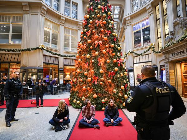 Polizisten stehen um Mitglieder der Protestgruppe „Letzte Generation“· vor einem mit Farbe besprühten Weihnachtsbaum in der Mädler-Passage in Leipzig.