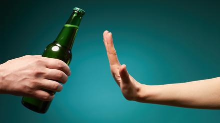 Eine grüne Bierflasche trifft auf eine ablehnende Hand.