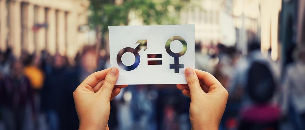 Gender equality concept as woman hands holding a white paper sheet with male and female symbol over a crowded city street background. Sex sign as a metaphor of social issue.