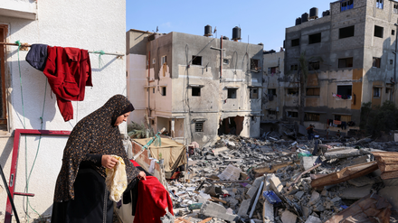 Eine palästinensische Frau hängt Wäsche vor ihrem zerstörten Haus auf. 