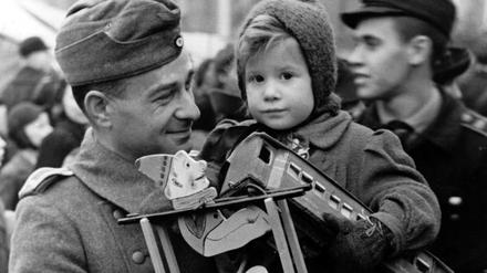 Unsere Mütter, unsere Väter. Ein Fronturlauber der Deutschen Wehrmacht trägt sein Kind über den Weihnachtsmarkt - im Berliner Lustgarten im Winter 1942. 