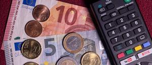 Die Summe von 18,94 Euro liegt auf einem Tisch neben der Fernbedienung für einen Fernseher. Der Rundfunkbeitrag soll ab 2025 vorläufigen Berechnungen von Finanzexperten zufolge um 58 Cent steigen. 