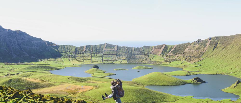 Full length of couple kissing while standing near lake and mountains against clear sky on sunny day, Corvo, Azores, Portugal model released Symbolfoto FVSF00236 