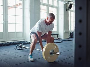Ein älterer Mann trainiert mit einer Langhantel in einem Fitnessstudio seine Rückenmuskulatur.