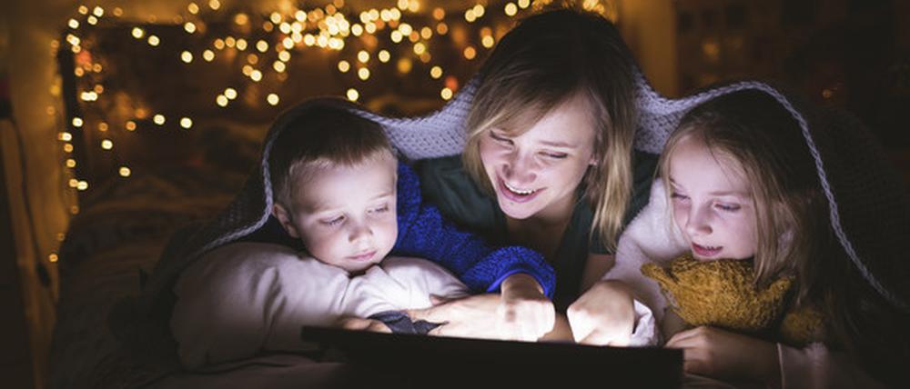 Mutter und Kinder unter der Decke mit digitaler Tablette