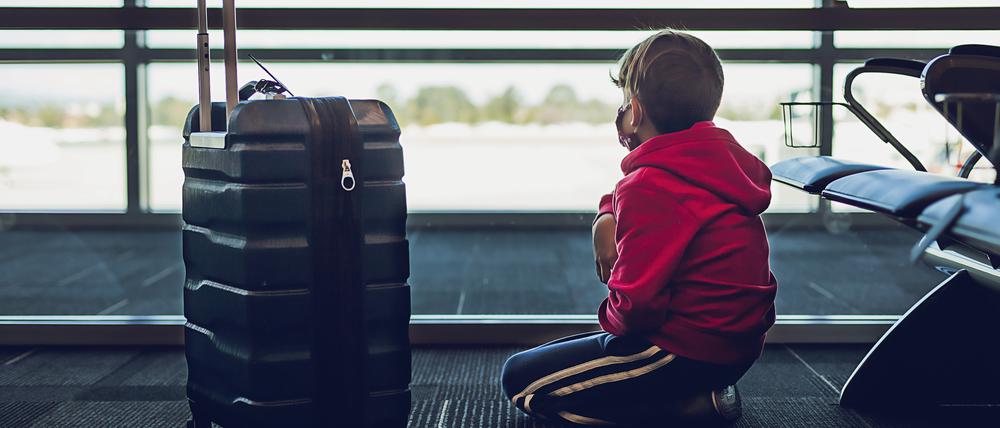 Young Boy Next To Suitcase Looking Out The Window At Airport.