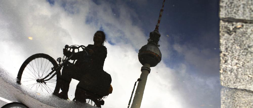 Radfahrerin spiegelt sich in Pfütze mit Fernsehturm am Alexanderplatz, Berlin.