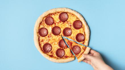 Obenansicht einer Peperoni-Pizza und einer Hand, die ein Stück Pizza schnappt.