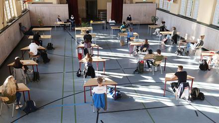 Schüler mit Mundschutz sitzen bei der Prüfungsvorbereitung fürs Abitur in einer zum Schulraum umfunktionierten Turnhalle.