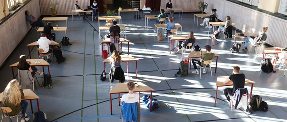 Schüler mit Mundschutz sitzen bei der Prüfungsvorbereitung fürs Abitur in einer zum Schulraum umfunktionierten Turnhalle.