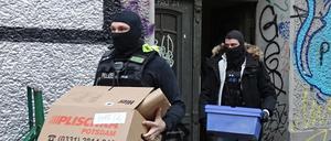 Polizeibeamte tragen während einer Durchsuchungsaktion Kartons aus einem Mietshaus.