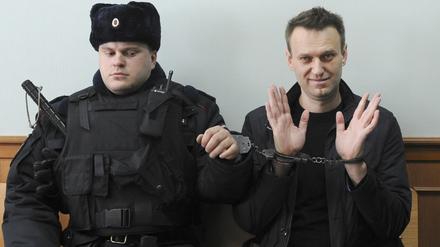 Der russische Oppositionsführer Alexej Nawalny (r) winkt für die Presse, während er in Handschellen vor Gericht sitzt. Der russische Oppositionspolitiker Alexej Nawalny ist nach Angaben der Justiz in Haft gestorben. Das teilte die Gefängnisverwaltung des nordrussischen Gebietes Jamal nach Angaben der Agentur Tass mit.