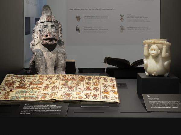 Ausstellungsansicht aus dem Stabi Kulturwerk „Manuscripta americana“. Der Gott Quetzalcoatl, Grünfederschlange und Erfinder der Schrift, verschmilzt hier mit Ehecatl, Wind (links). Daneben ein Affe aus Alabaster aus der Teotihuacan-Kultur (rechts). Foto: SBB-PK/2022
