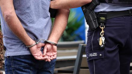 Ein Mann steht in Handschellen neben einem Polizisten. 