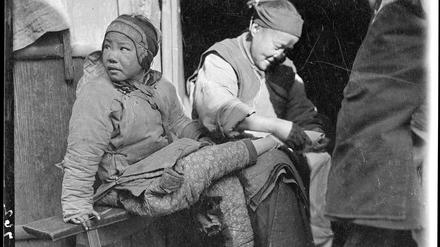 US-Fotograf Sidney D. Gamble beobachtet 1919 eine Alltagsszene in China. Eine Frau bindet einem Mädchen die Füße. 