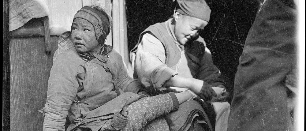 US-Fotograf Sidney D. Gamble beobachtet 1919 eine Alltagsszene in China. Eine Frau bindet einem Mädchen die Füße. 