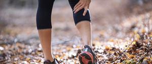 Sportswoman having cramp in leg while standing on forest path model released Symbolfoto JSRF01246