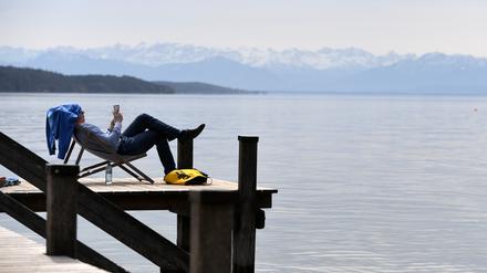 Ein Mann liegt in einem Liegestuhl auf einem Steg am Starnberger See.