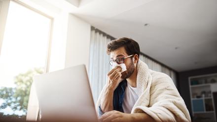 Shot of a sickly young businessman blowing his nose with a tissue while working from home