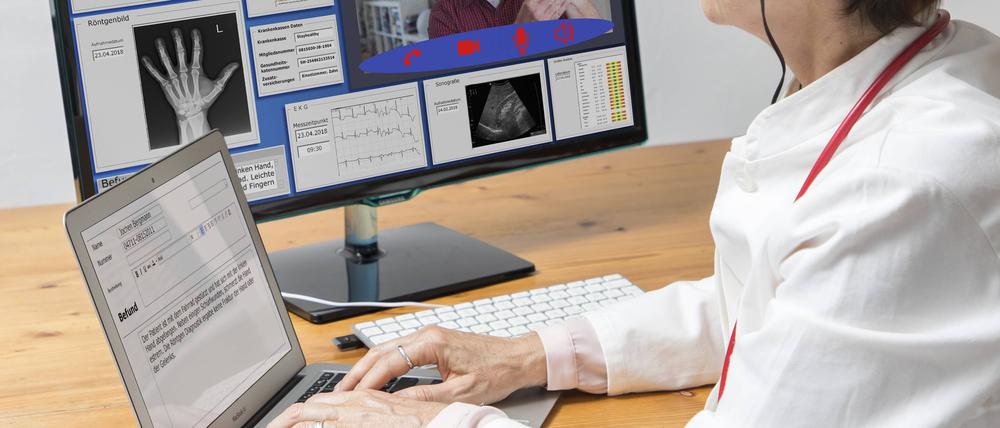 Eine Ärztin in einer Praxis, kommuniziert mit dem Patienten über eine Webcam, Patientendaten und Befunde auf dem Monitor  