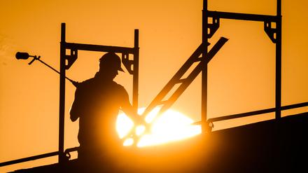 Ein Bauarbeiter steht mit einem Gasbrenner beim Bau eines Mehrfamilienhauses im Neubaugebiet Kronsrode, als am Horizont die Sonne aufgeht.  