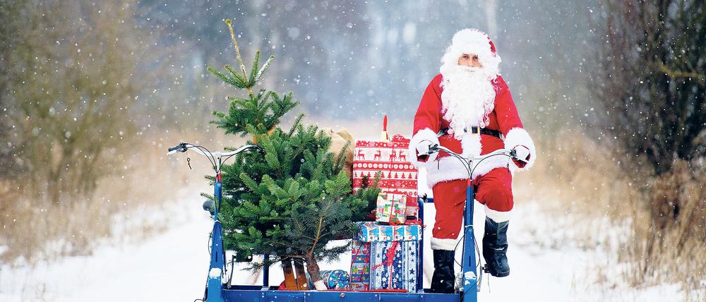 Mit einer Fahrraddraisine der Erlebnisbahn, beladen mit Geschenken, Ski und einem Weihnachtsbaum, ist ein Weihnachtsmann in Mellensee (Brandenburg) unterwegs.