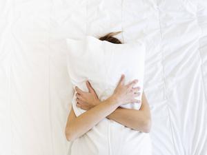 Eine Frau liegt rücklings auf dem Bett und umklammert ihr Kopfkissen.
