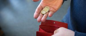 Münzen im Wert von fünf Euro liegen in einer Hand über einem Portemonnaie. 
