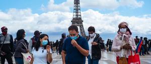Passanten tragen am Platz Trocadero in der Nähe des Eiffelturms Mundschutze und Gesichtsmasken.