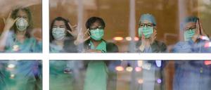 Mit Mundschutz stehen medizinische Mitarbeiter hinter einer Glasscheibe