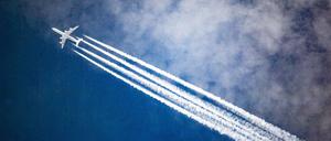 Ein Flugzeug zieht Kondensstreifen hinter sich her, während es durch die Wolken fliegt. 