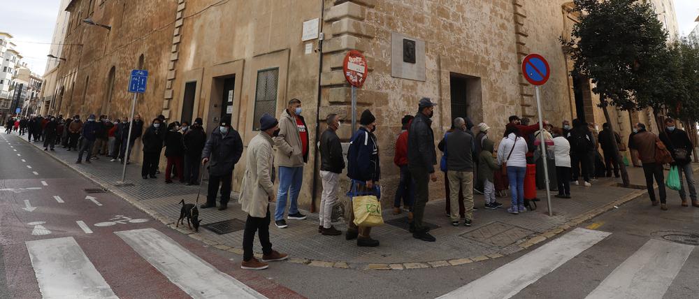 Menschen in Palma de Mallorca warten in einer Schlange, um ein Wohltätigkeits-Weihnachtsessen für arme und obdachlose Menschen in der Caputxins-Kirche zu bekommen.